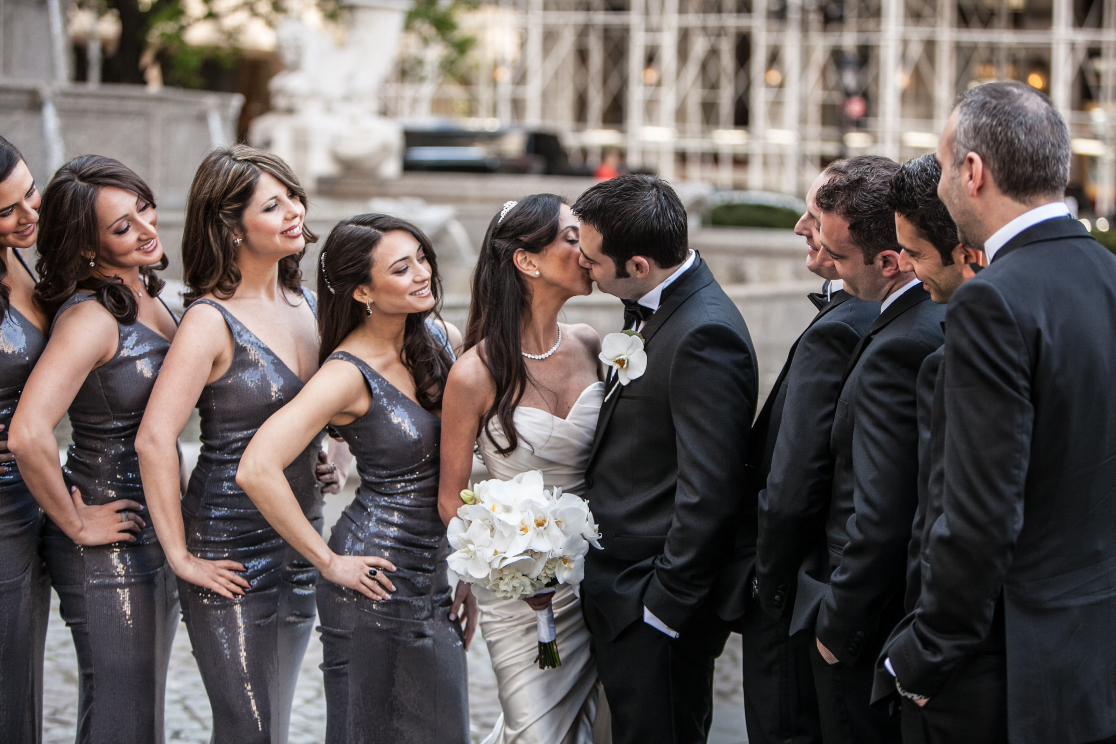 Bride and groom kissing with bridal party watching
